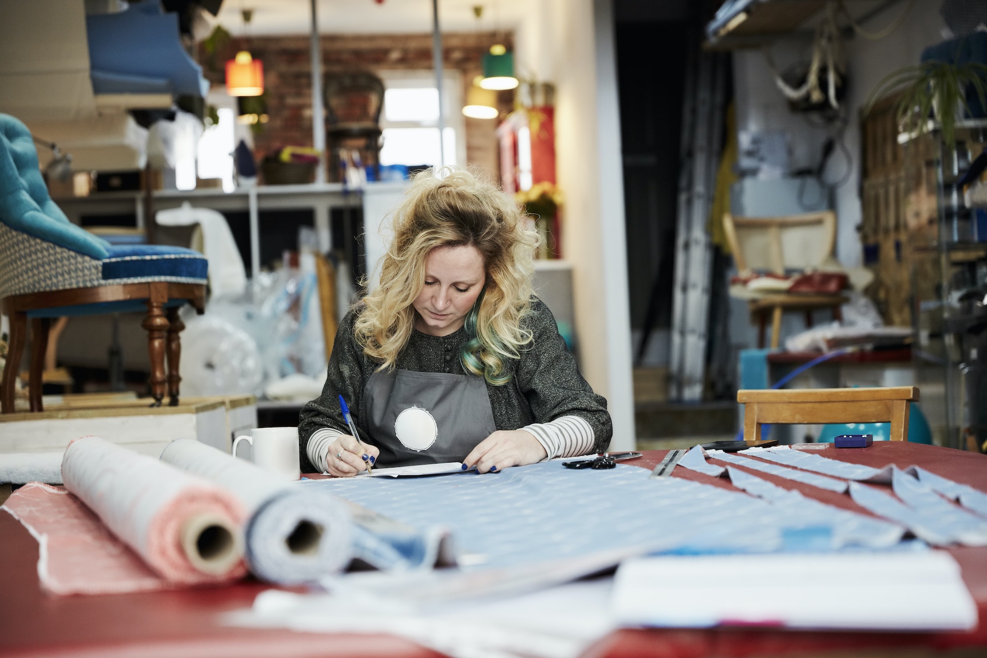 A woman preparing, measuring and cutting upholstery fabric on a workbench.