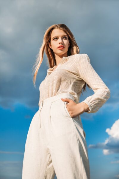 bottom view of elegant fashionable model posing in white stylish clothes with cloudy sky on